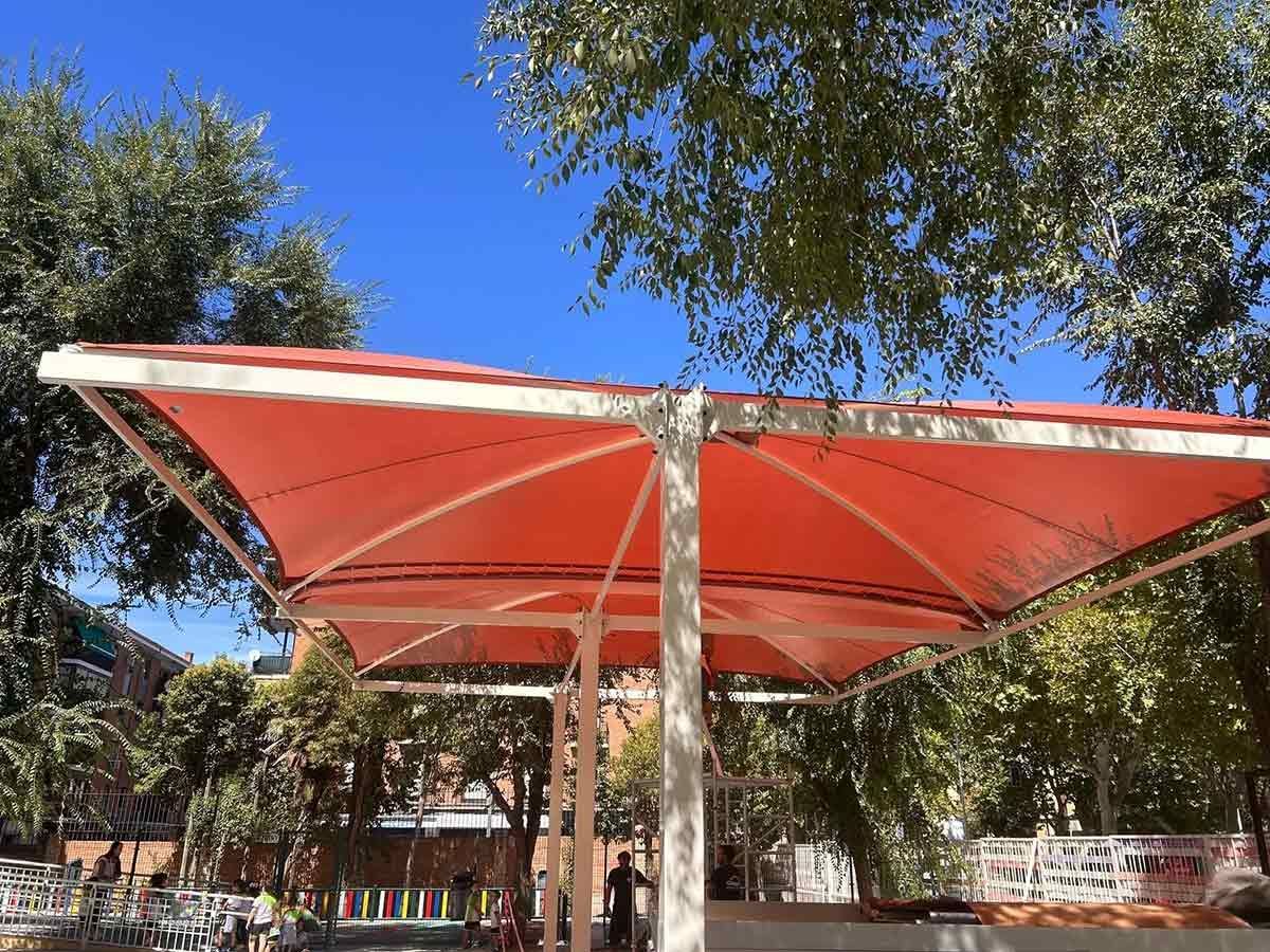 Estructura de sombra naranja en un parque con árboles y un cielo azul.