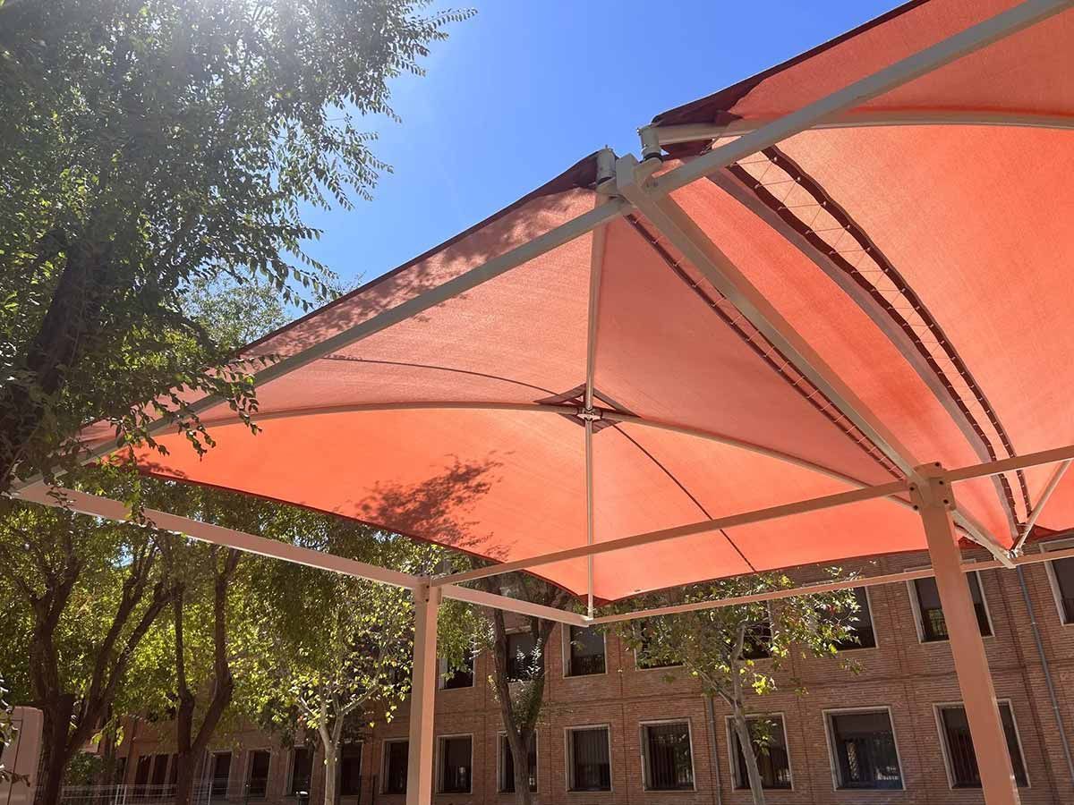 Dosel naranja que proporciona sombra al aire libre, visible contra un cielo azul, cerca de un edificio y árboles.