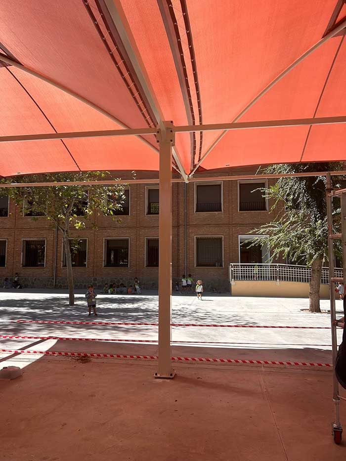 Dosel rojo sobre un área al aire libre, con un edificio al fondo.