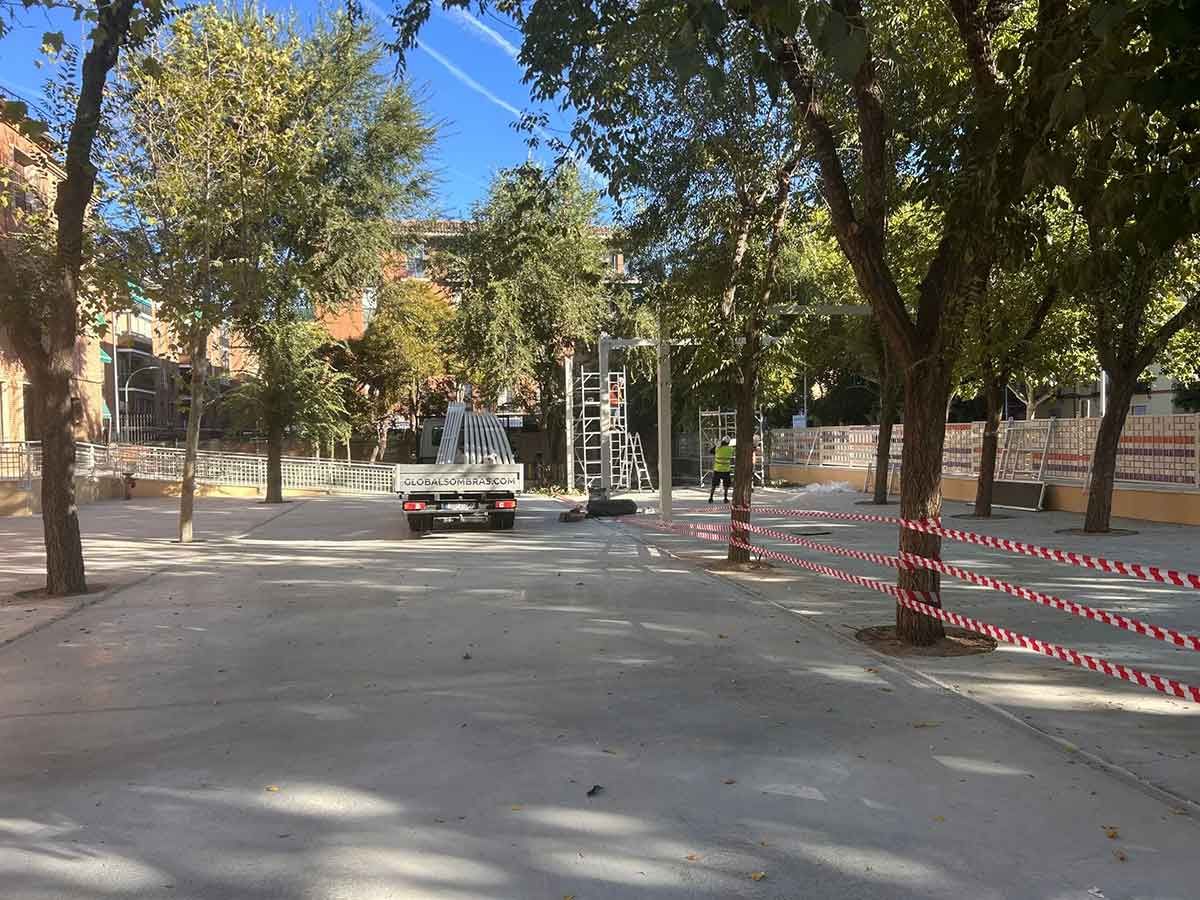 Parque con árboles, un camión y equipo de construcción; cinta roja y blanca rodea algunos árboles.