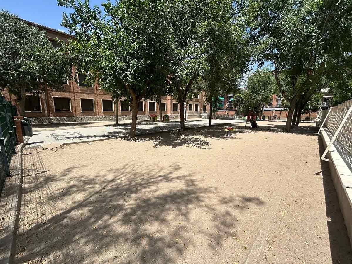 Patio de arena con árboles frente a un edificio de ladrillo.