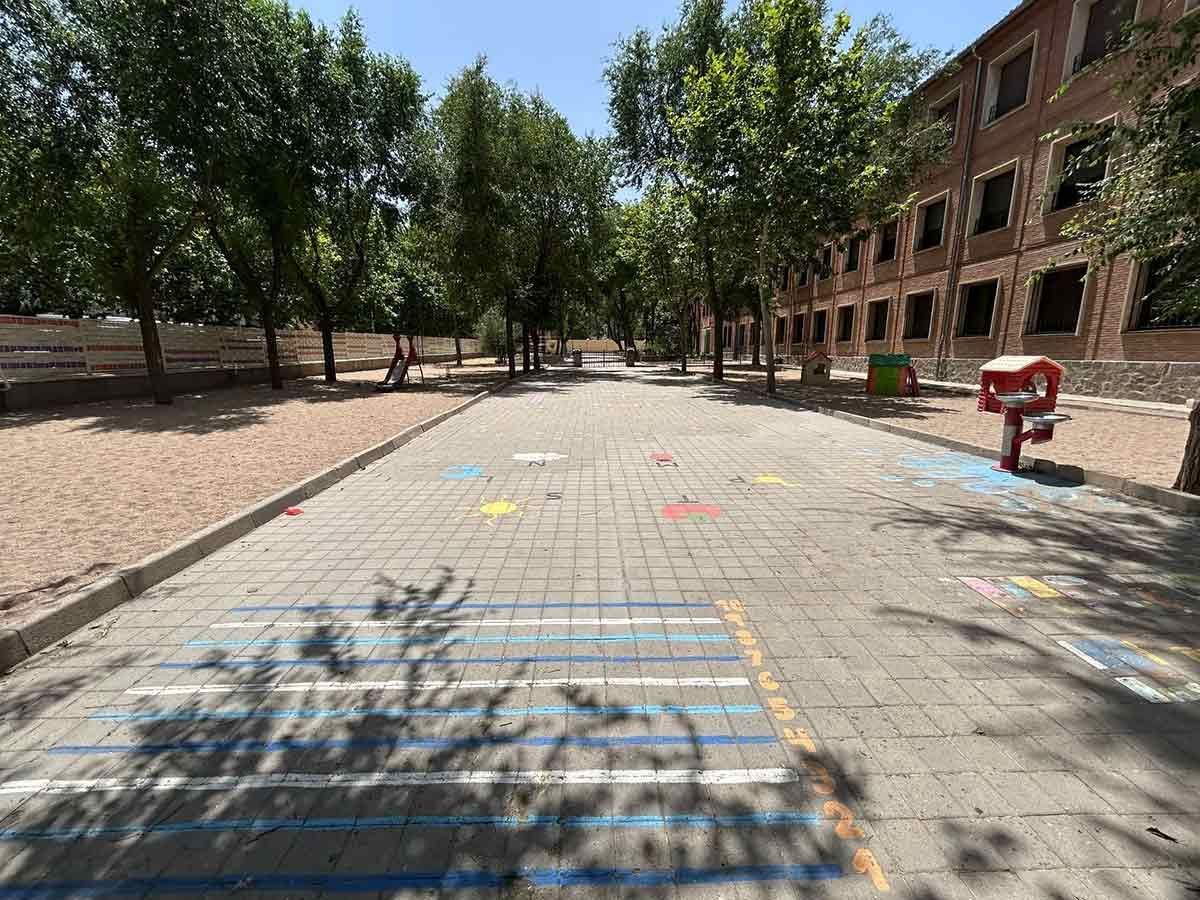 Camino pavimentado con árboles a ambos lados que conduce a un edificio de ladrillo. Formas coloridas pintadas en el suelo.