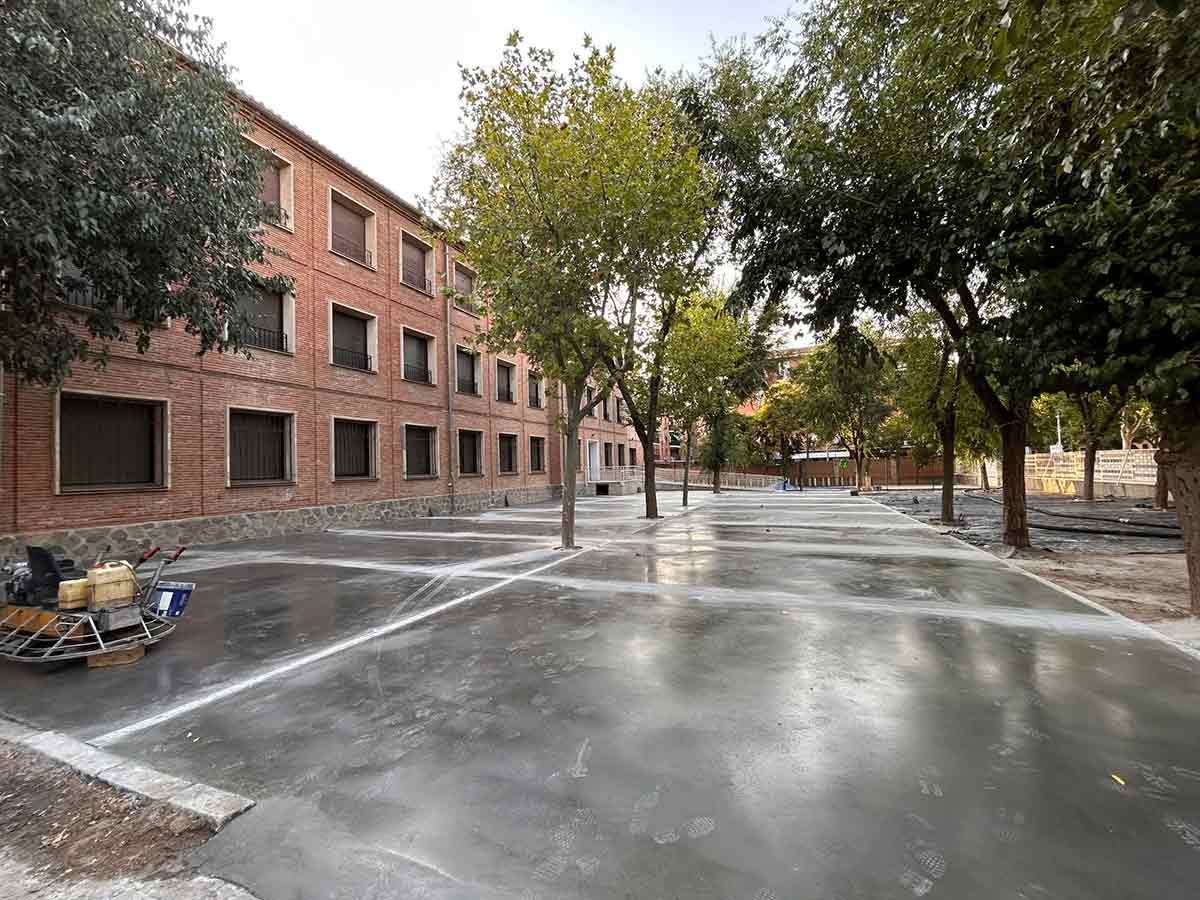 Edificio de ladrillo con árboles a lo largo de una zona pavimentada. Pavimento mojado, probablemente limpiado recientemente.