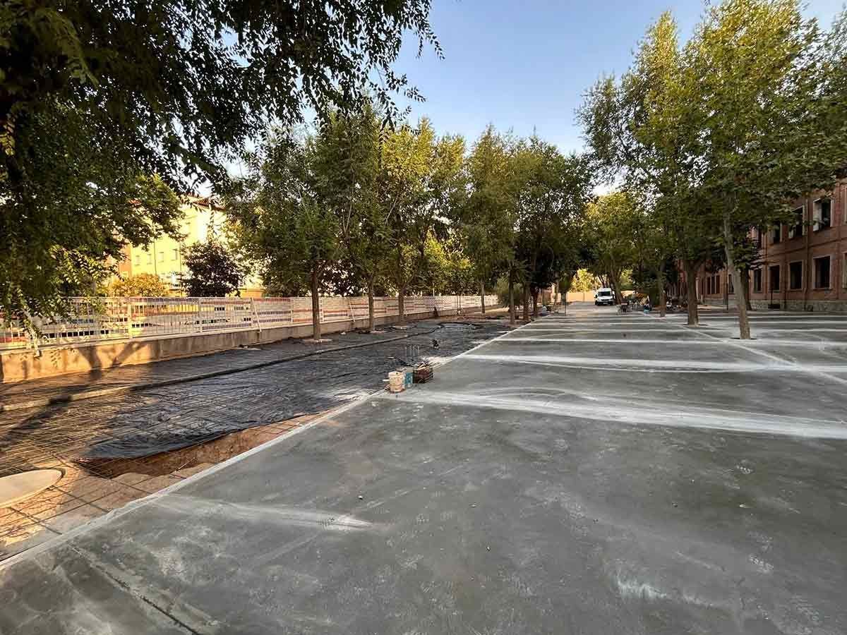 Camino de hormigón junto a una zona arbolada con un edificio a la derecha.