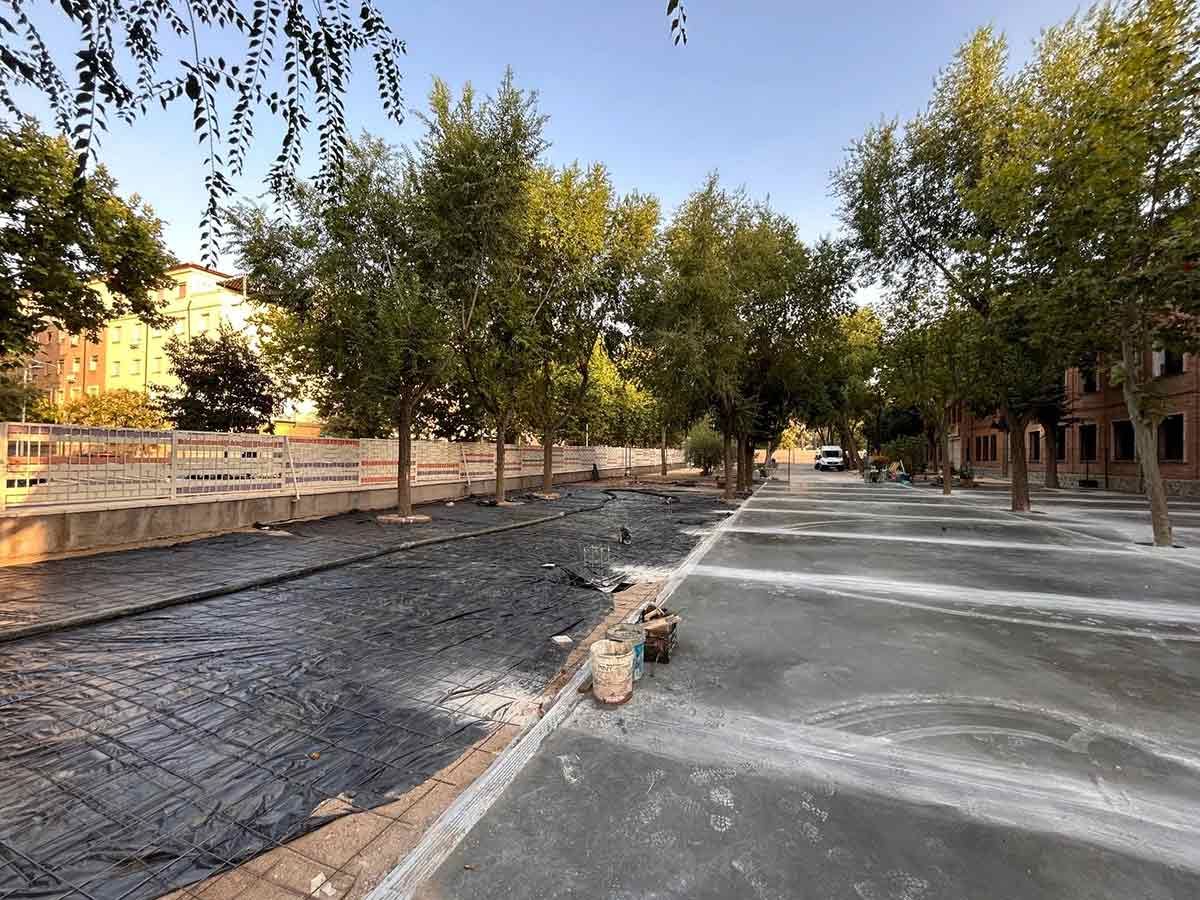 Los árboles bordean un sendero gris junto a un canal seco y negro. Se ven edificios y el cielo.