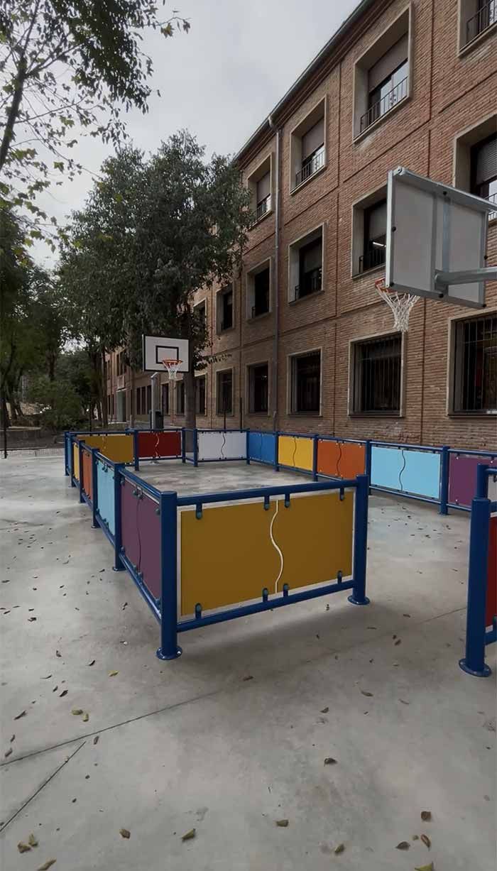 Cancha de baloncesto con vallas de colores frente a un edificio de ladrillos en un día nublado.