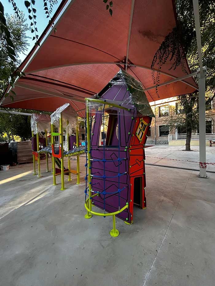 Estructura de juegos con elementos de color morado, rojo y amarillo bajo una estructura de sombra roja.