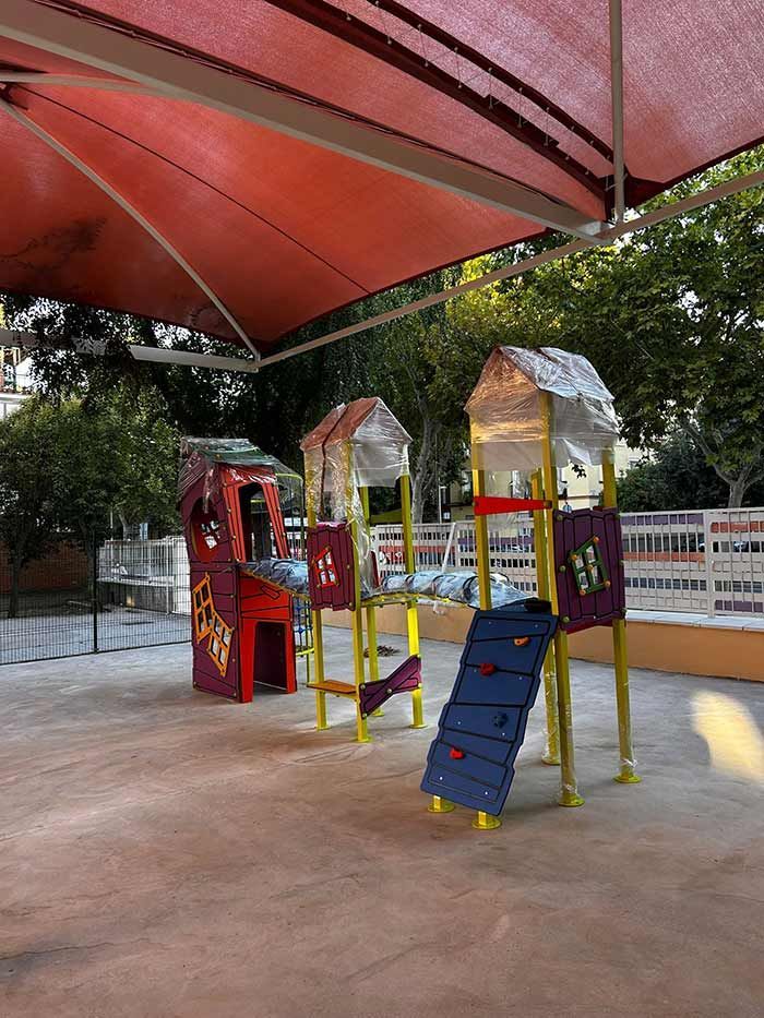 Parque infantil con estructuras de juego coloridas bajo una sombrilla roja.