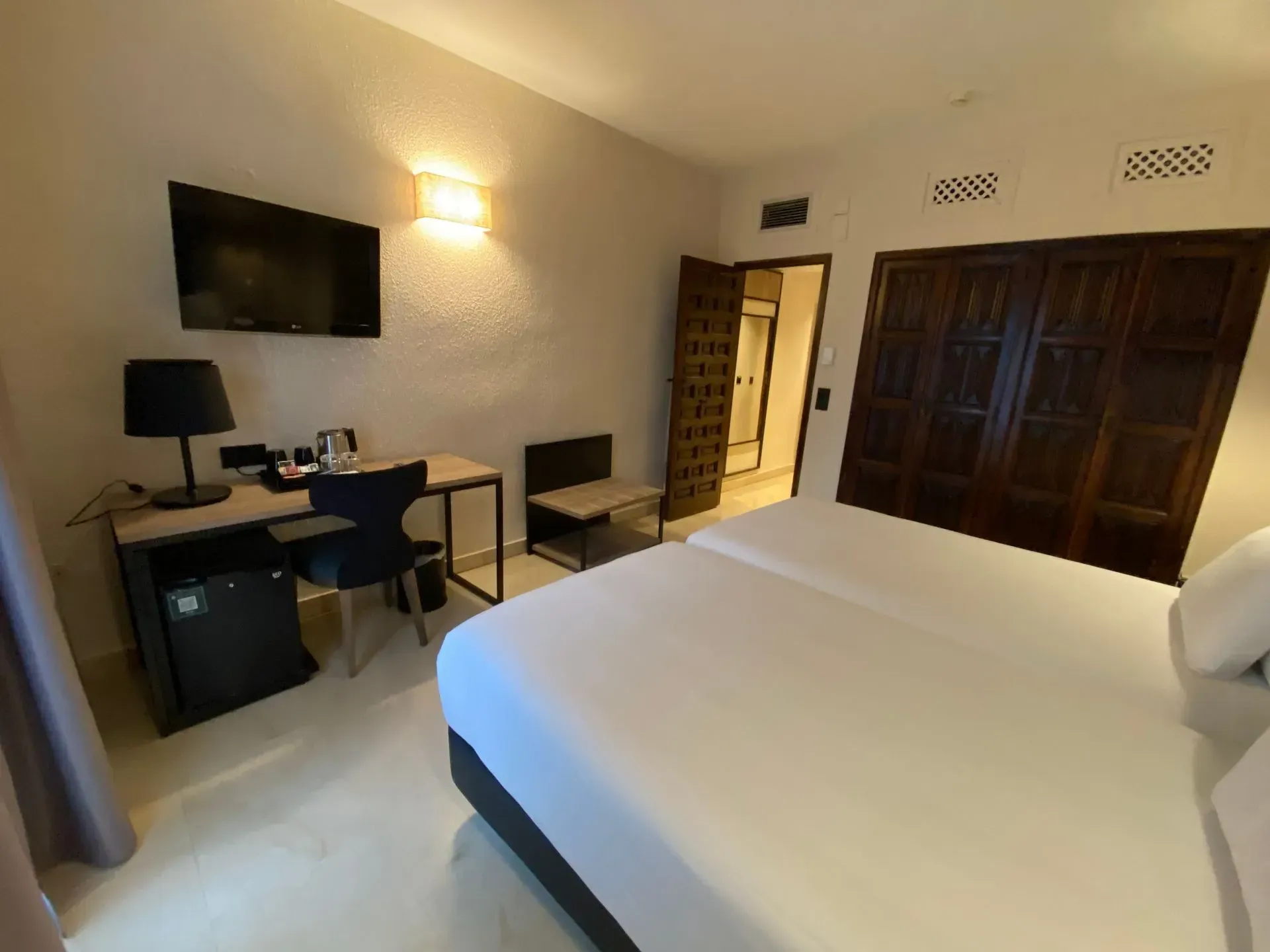 Habitación de hotel con dos camas, escritorio con TV, silla y entrada al baño.