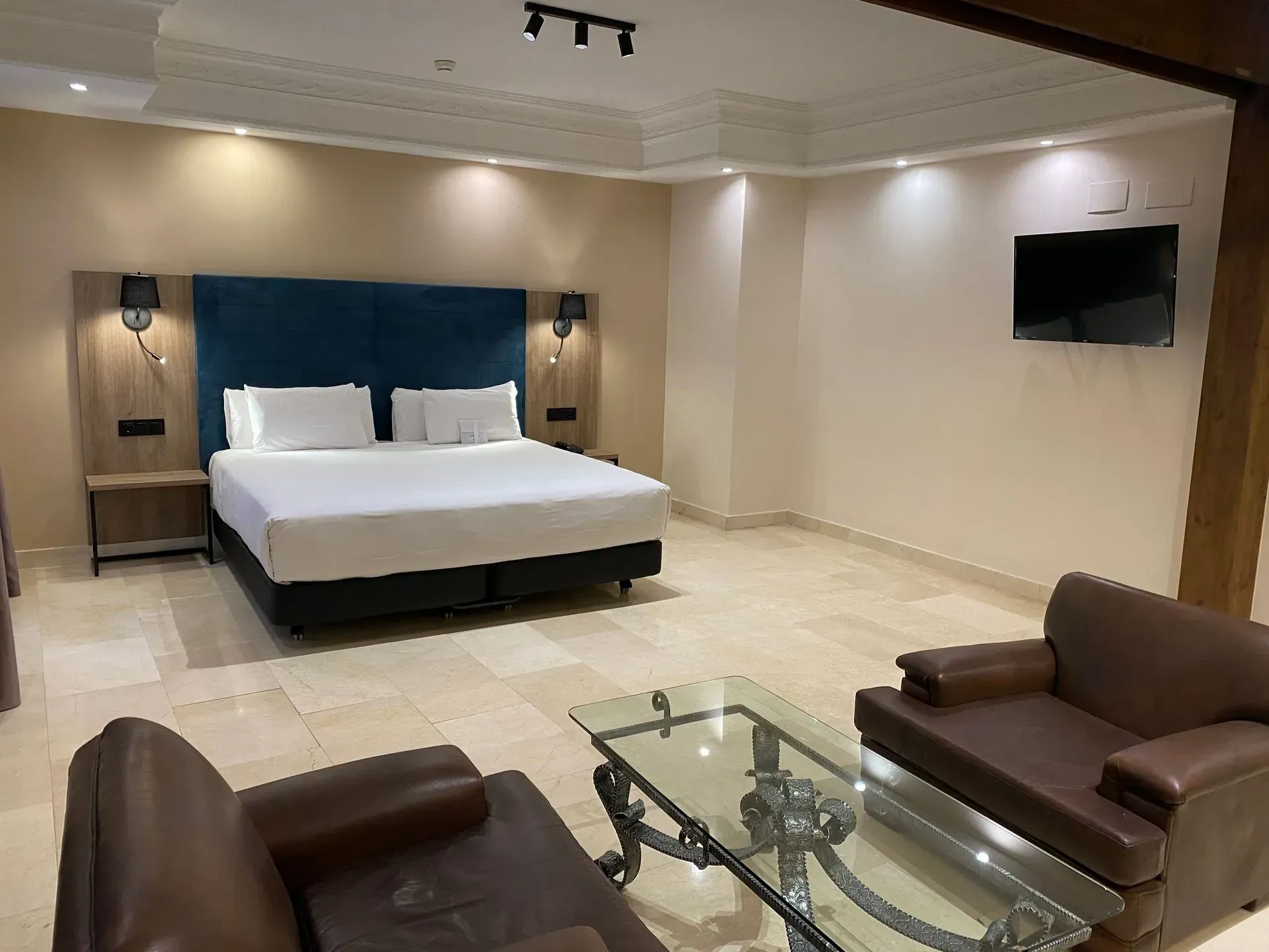 Habitación de hotel con cama, zona de estar con dos sillas de cuero marrón y mesa de café.