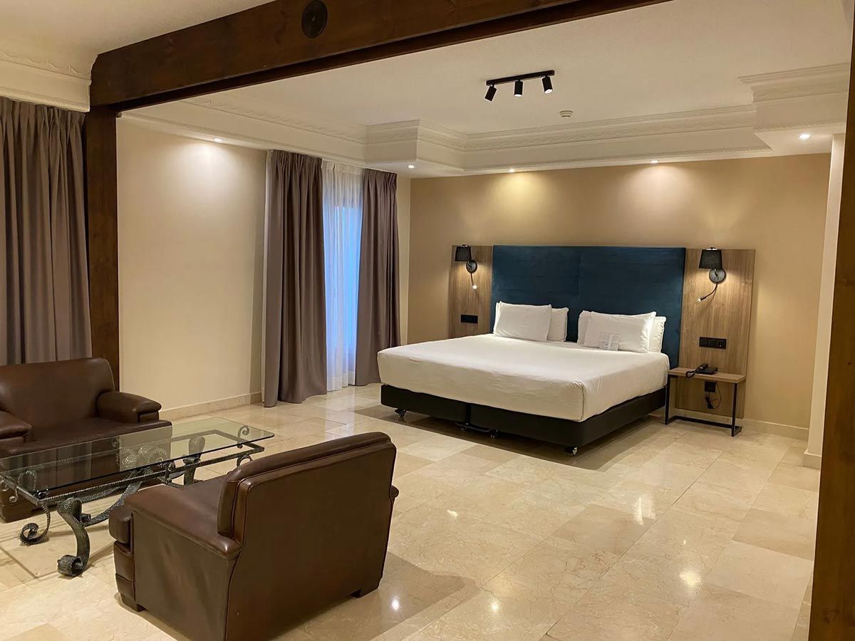 Suite de hotel con cama King, dos sillones de cuero, mesa de café y piso de mármol.