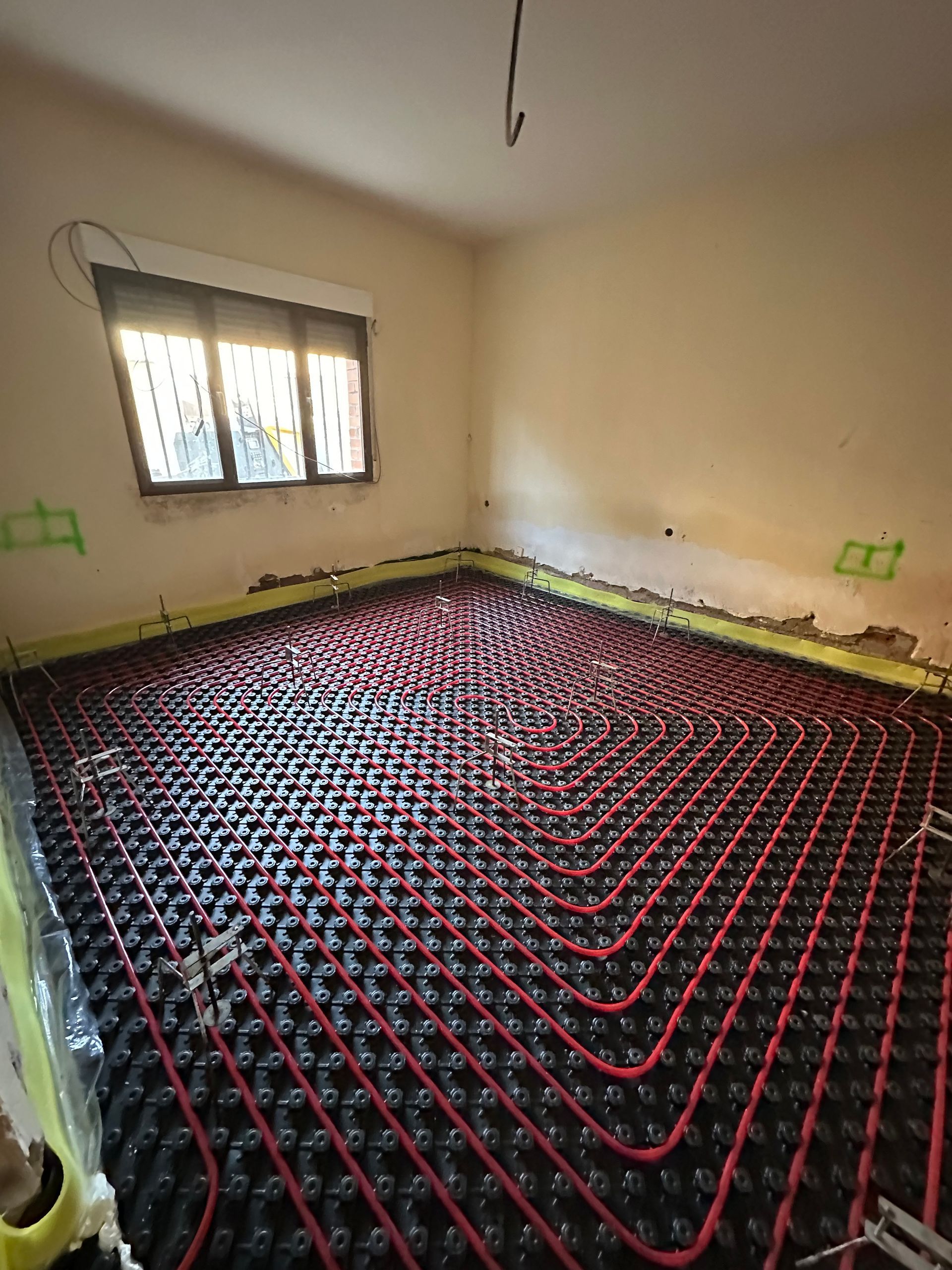Habitación con tubos de calefacción por suelo radiante de color rojo instalados sobre aislamiento negro antes de colocar el suelo.