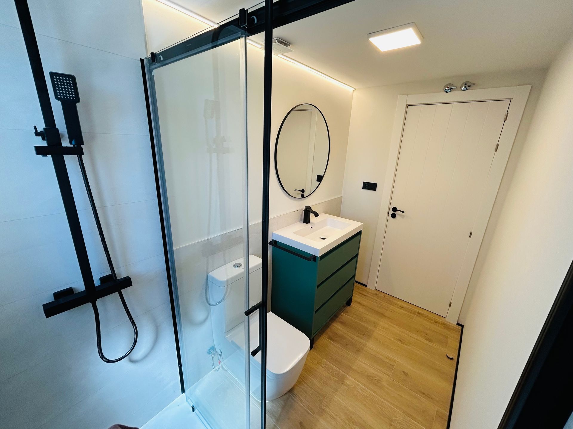 Baño moderno con accesorios de ducha negros, tocador verde e inodoro blanco.