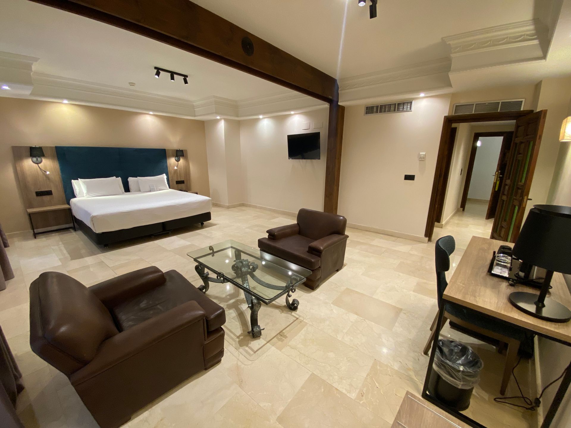 Suite de hotel con cama, zona de estar, escritorio y puerta abierta a otra habitación.