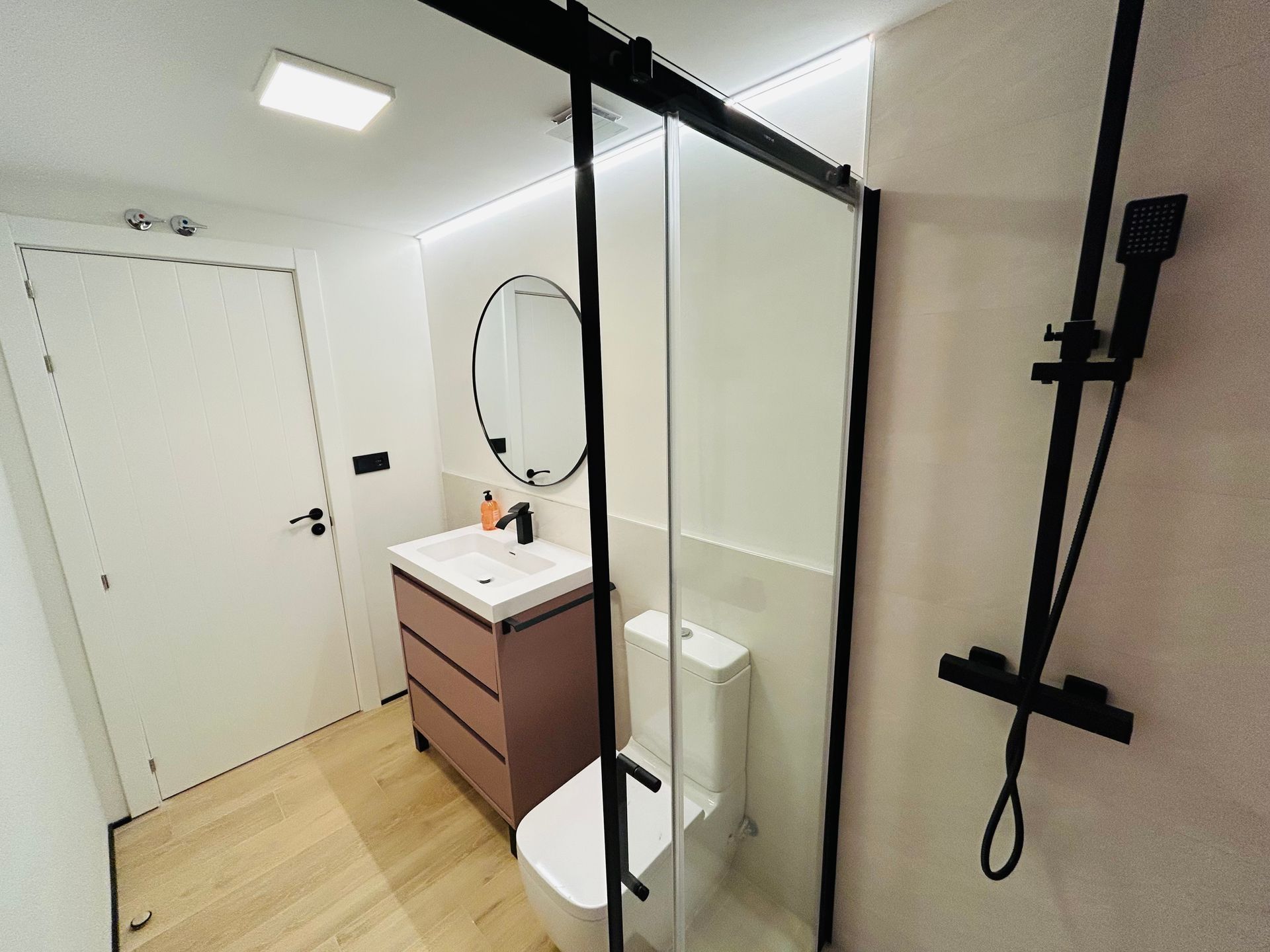 Baño moderno con puerta de ducha corrediza de vidrio, tocador rosa y accesorios negros.