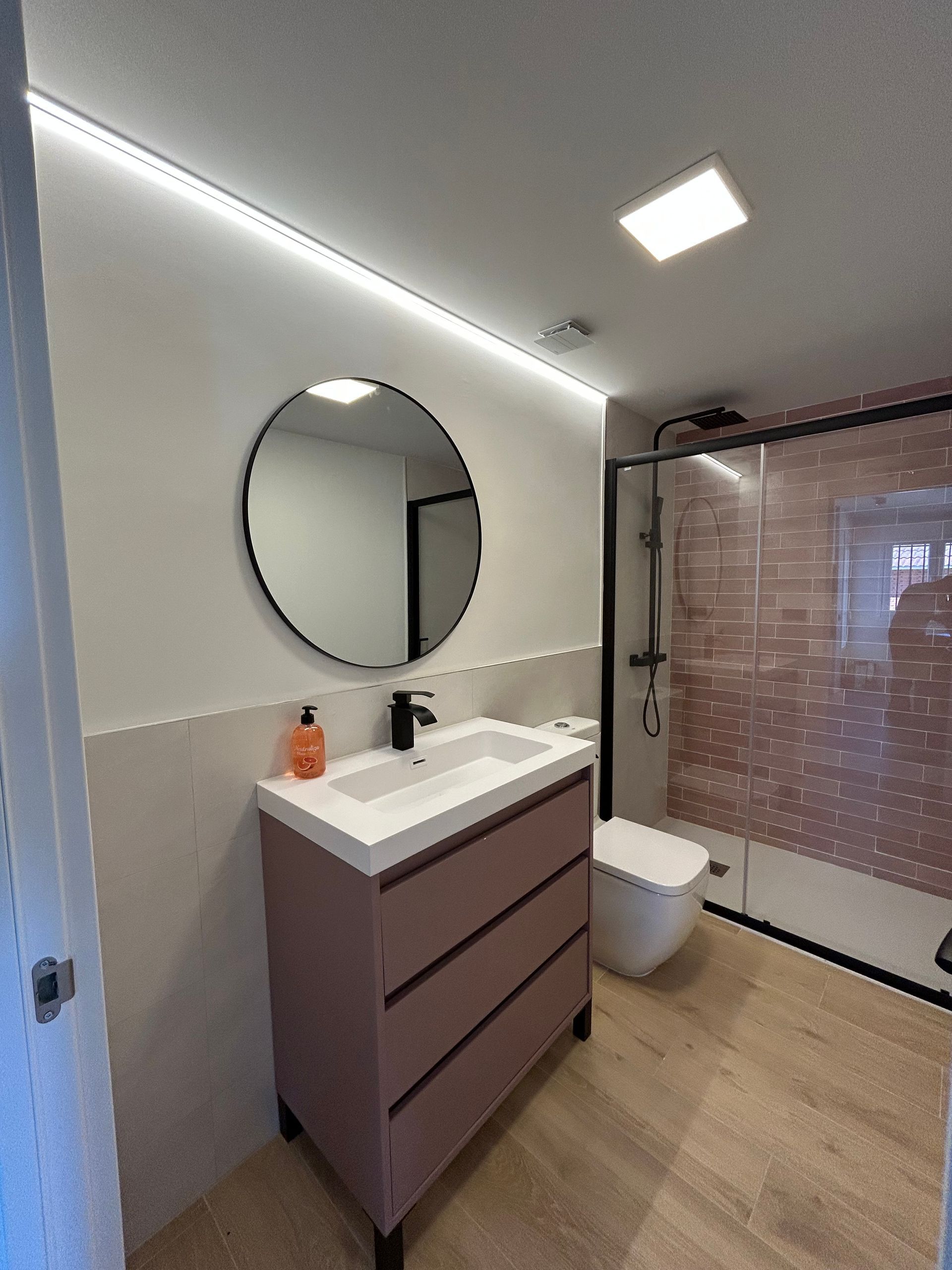 Baño moderno con tocador malva, espejo redondo y ducha a ras de suelo.