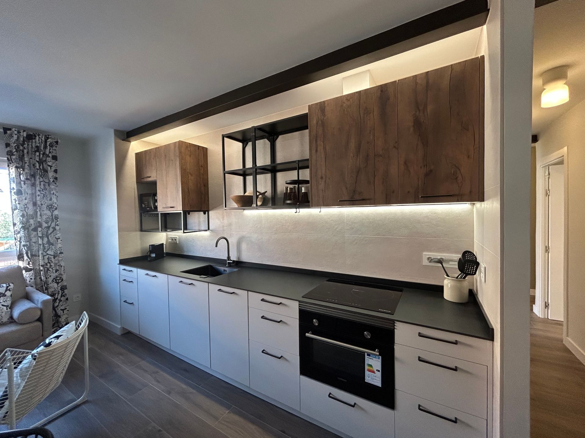 Cocina moderna con gabinetes blancos, encimeras oscuras y gabinetes superiores de madera.