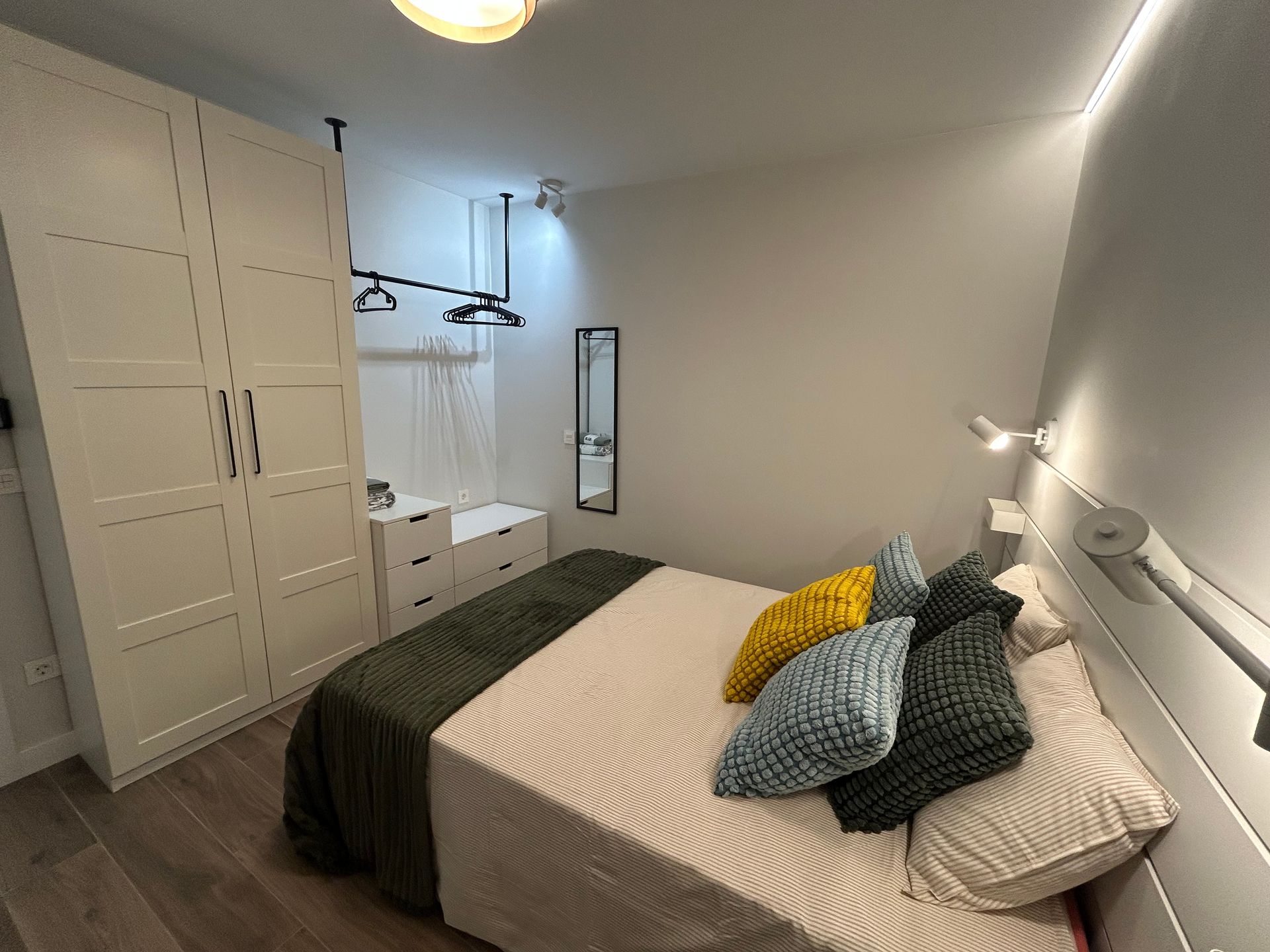 Dormitorio con armario blanco, cama con almohadas e iluminación lateral.