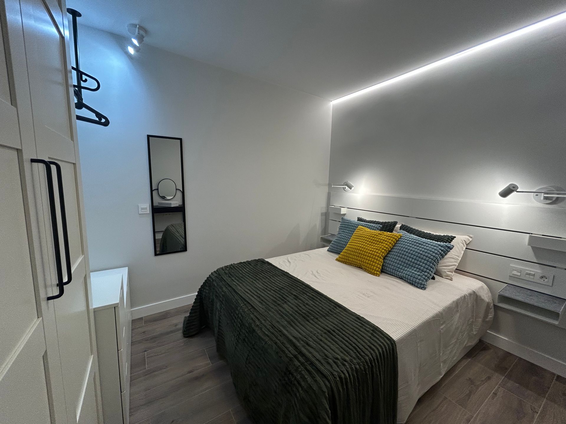Dormitorio con cama, almohadas y luces decorativas; se ven un armario y un espejo.