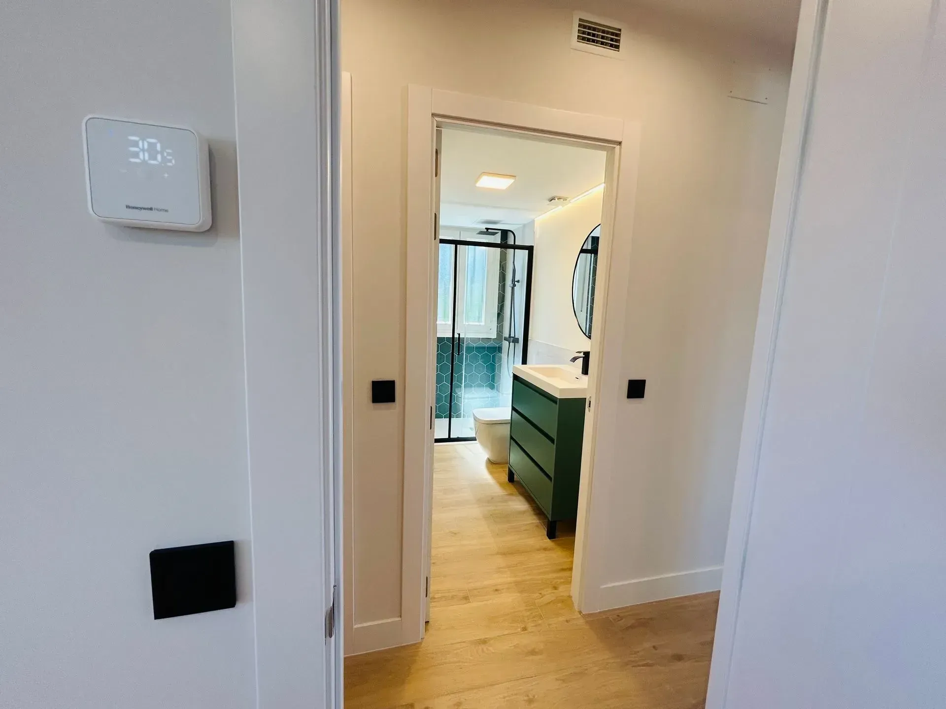 Pasillo con termostato y vista a un baño con tocador verde.