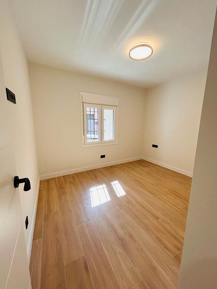 Habitación vacía con pisos de madera, una ventana y una luz de techo.