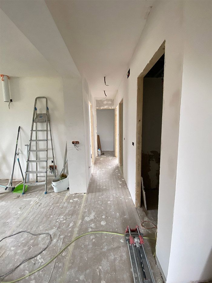 Pasillo en reforma con paredes blancas, suelo sin acabar y herramientas.