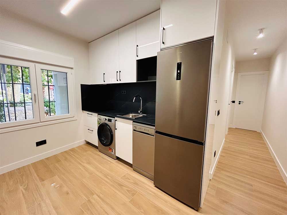Cocina moderna con gabinetes blancos, electrodomésticos de acero inoxidable y pisos de madera.