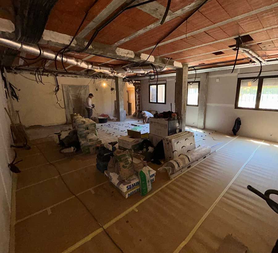 Habitación interior en construcción, con techo visto, materiales en el suelo y un obrero visible al fondo.