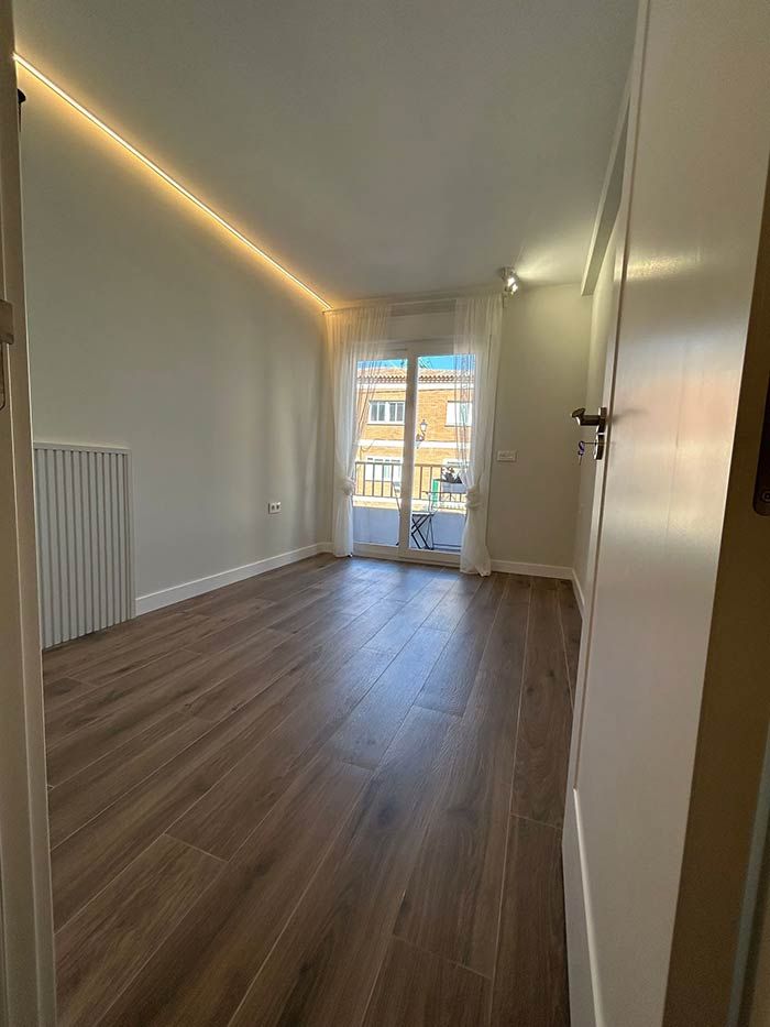 Habitación vacía con suelo de madera, balcón e iluminación empotrada.