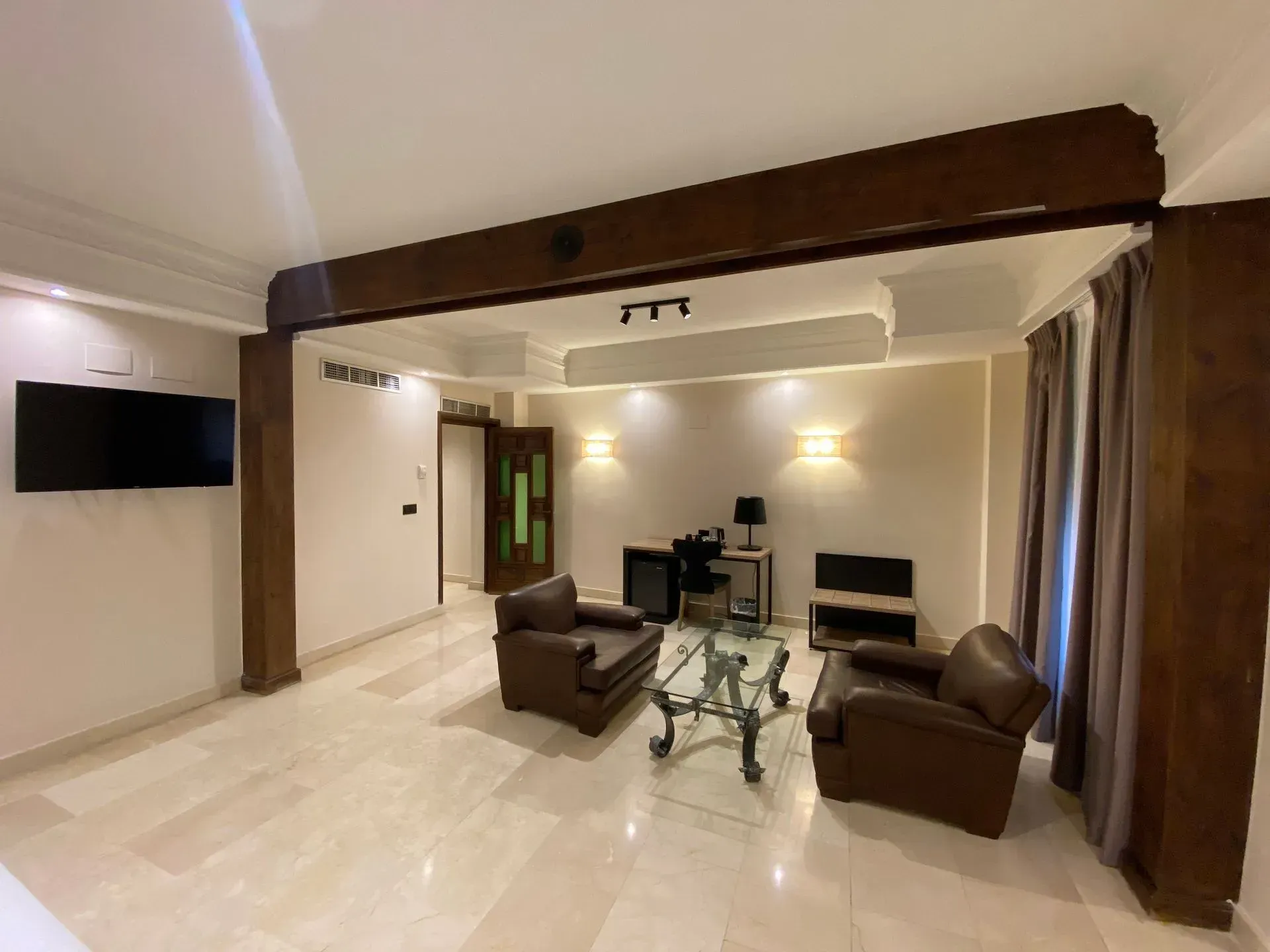 Sala de estar con sillones de cuero marrón, TV y mesa de centro de cristal bajo vigas de madera.