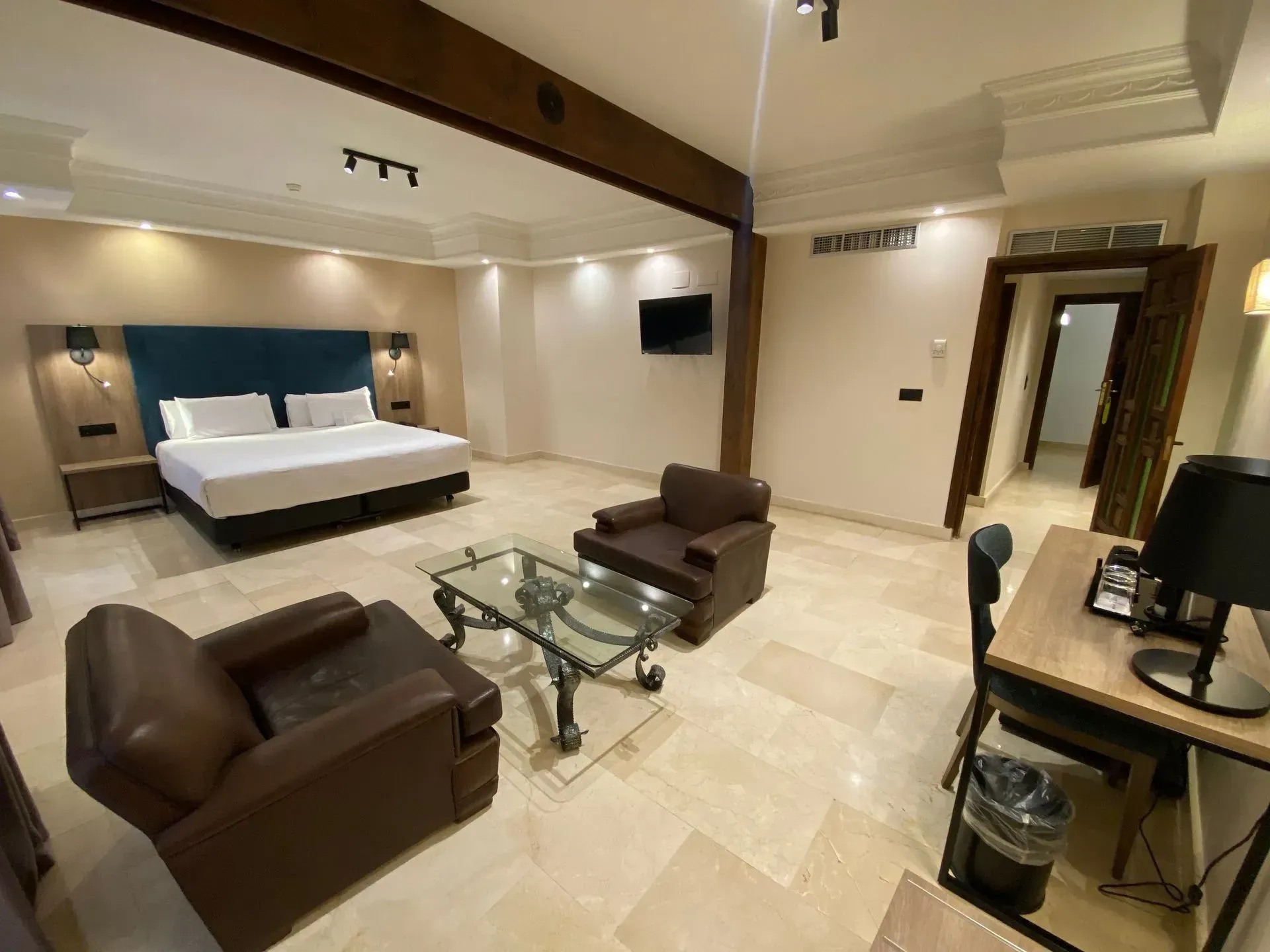 Habitación de hotel con una cama King, dos sillas, una mesa de vidrio y un escritorio.