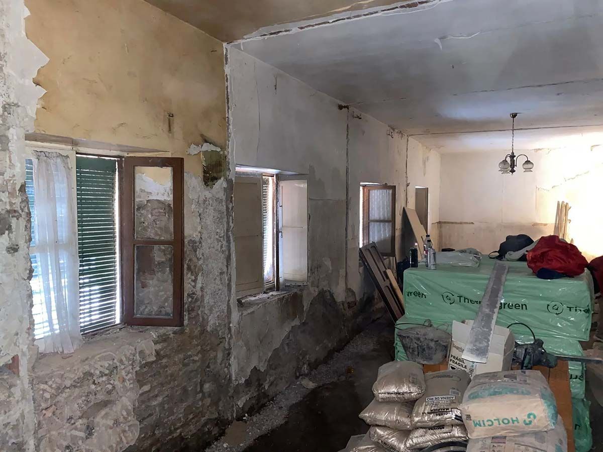 Interior de una habitación en reforma con ladrillo visto, ventanas y materiales de construcción.