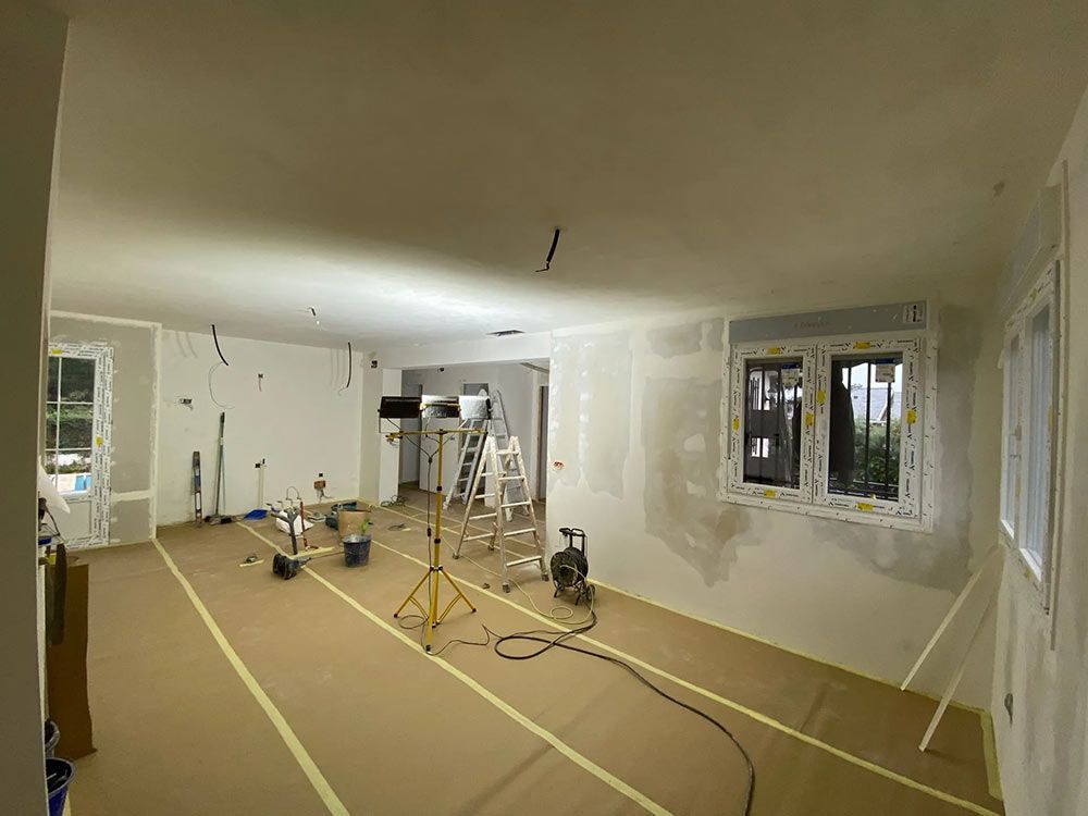 Habitación en reforma, con paredes imprimadas en blanco. Instalación eléctrica visible, escaleras y suelo protector.