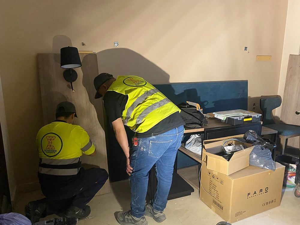 Dos personas con chalecos de seguridad instalando algo contra una pared de una habitación.