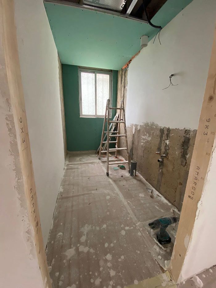 Reforma interior: recibidor con paredes vistas, escalera, ventana con techo verde y pared de acento.