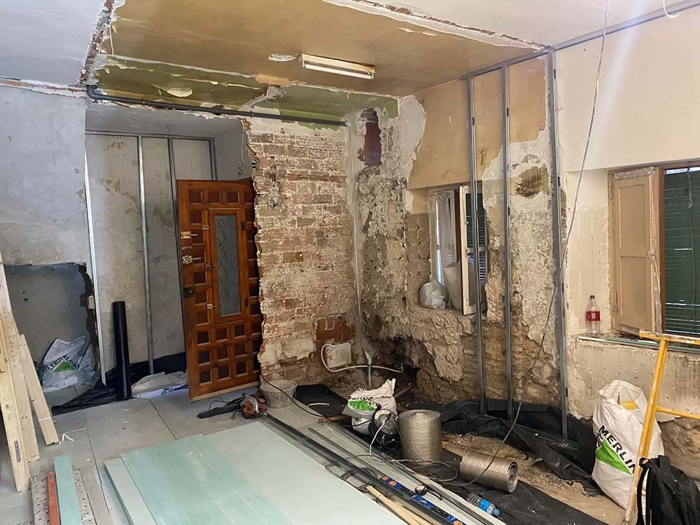 Habitación en reforma con ladrillo visto, vigas y materiales de construcción. Puerta y ventana visibles.