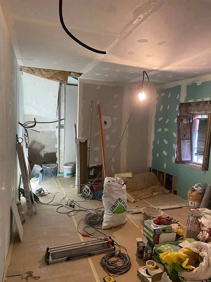 Habitación en construcción con paneles de yeso y cableado expuesto, herramientas y materiales esparcidos.