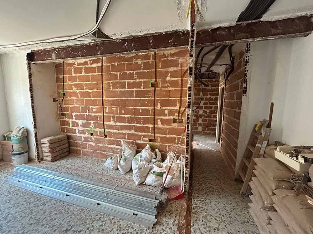 Interior en proceso de renovación, paredes de ladrillo visto, cableado eléctrico, materiales de construcción esparcidos por el suelo.