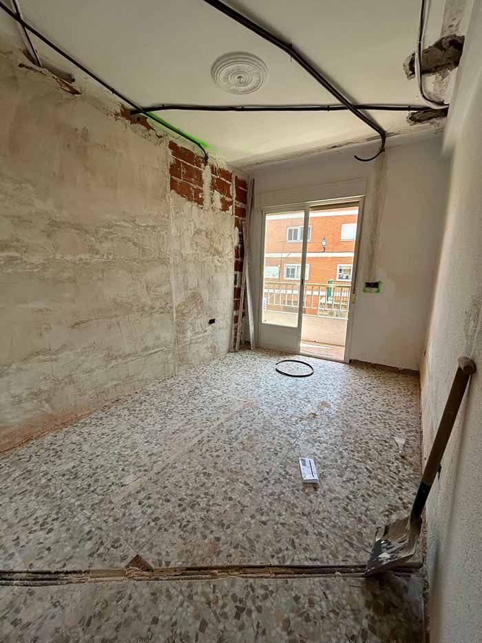 Habitación en reforma con ladrillo visto, suelo de hormigón, puerta abierta al exterior.