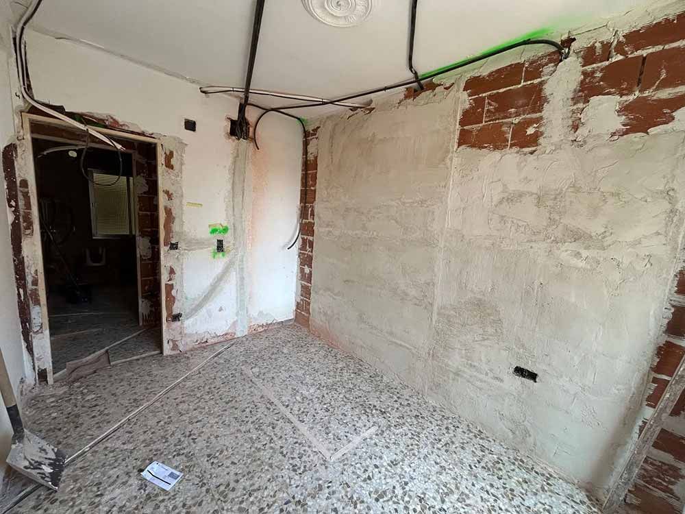 Habitación en construcción con ladrillo visto, cableado y paredes parcialmente enlucidas.