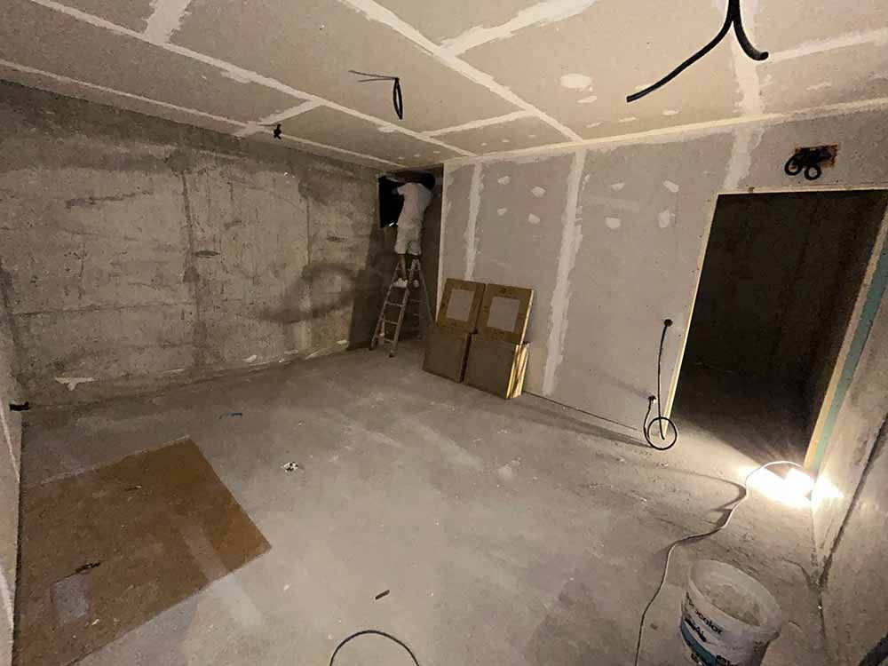 Habitación en construcción, paredes de concreto, paneles de yeso, persona en escalera trabajando en el techo.