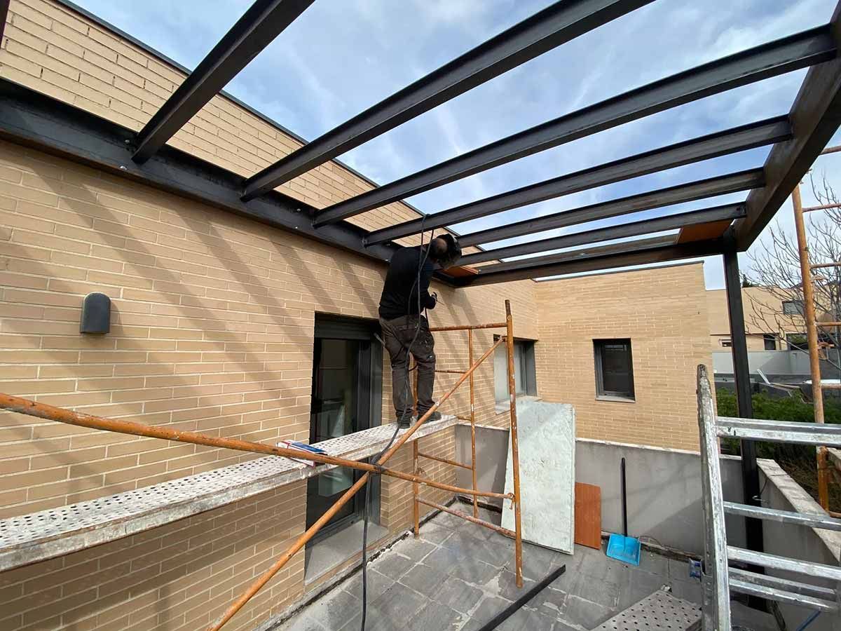 Obrero de la construcción en un andamio instalando una marquesina de metal en un edificio.