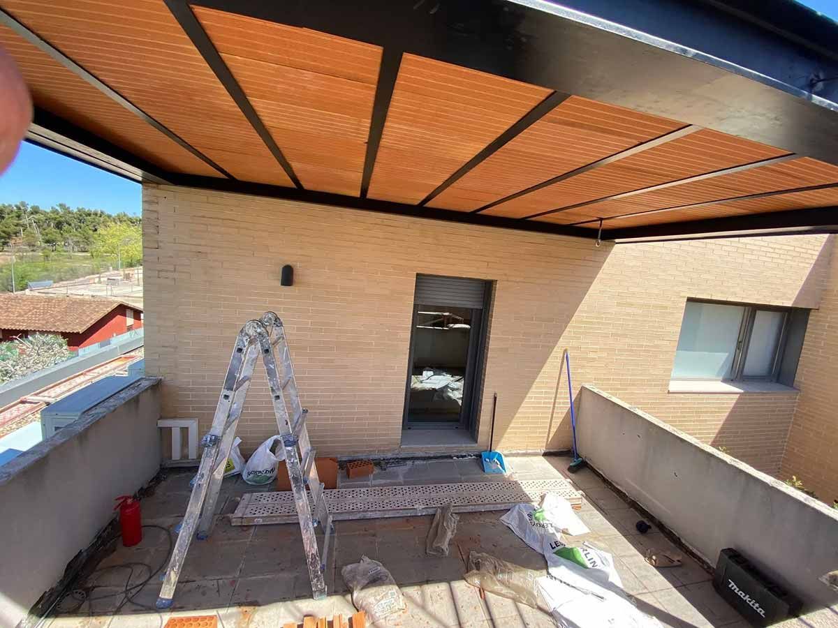 Terraza en construcción con fachada de ladrillo, techo de madera y escalera.
