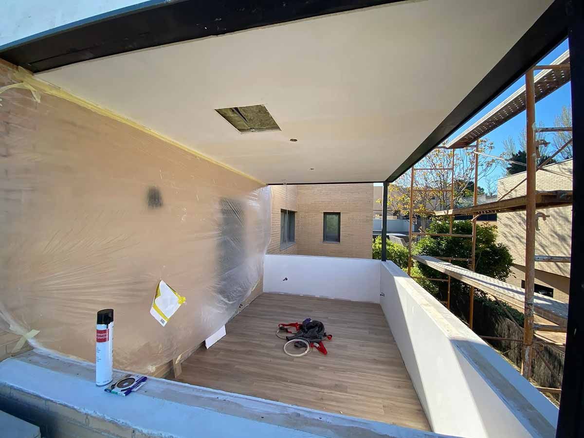 Un balcón cubierto en construcción. Las paredes están cubiertas de papel y hay herramientas en el suelo.