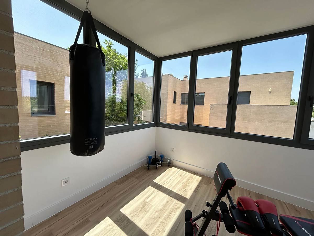 Saco de boxeo colgado en un gimnasio casero iluminado por el sol y con grandes ventanales.
