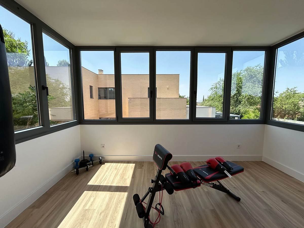 Gimnasio en casa con ventanas luminosas, banco de ejercicios, pesas y saco de boxeo.