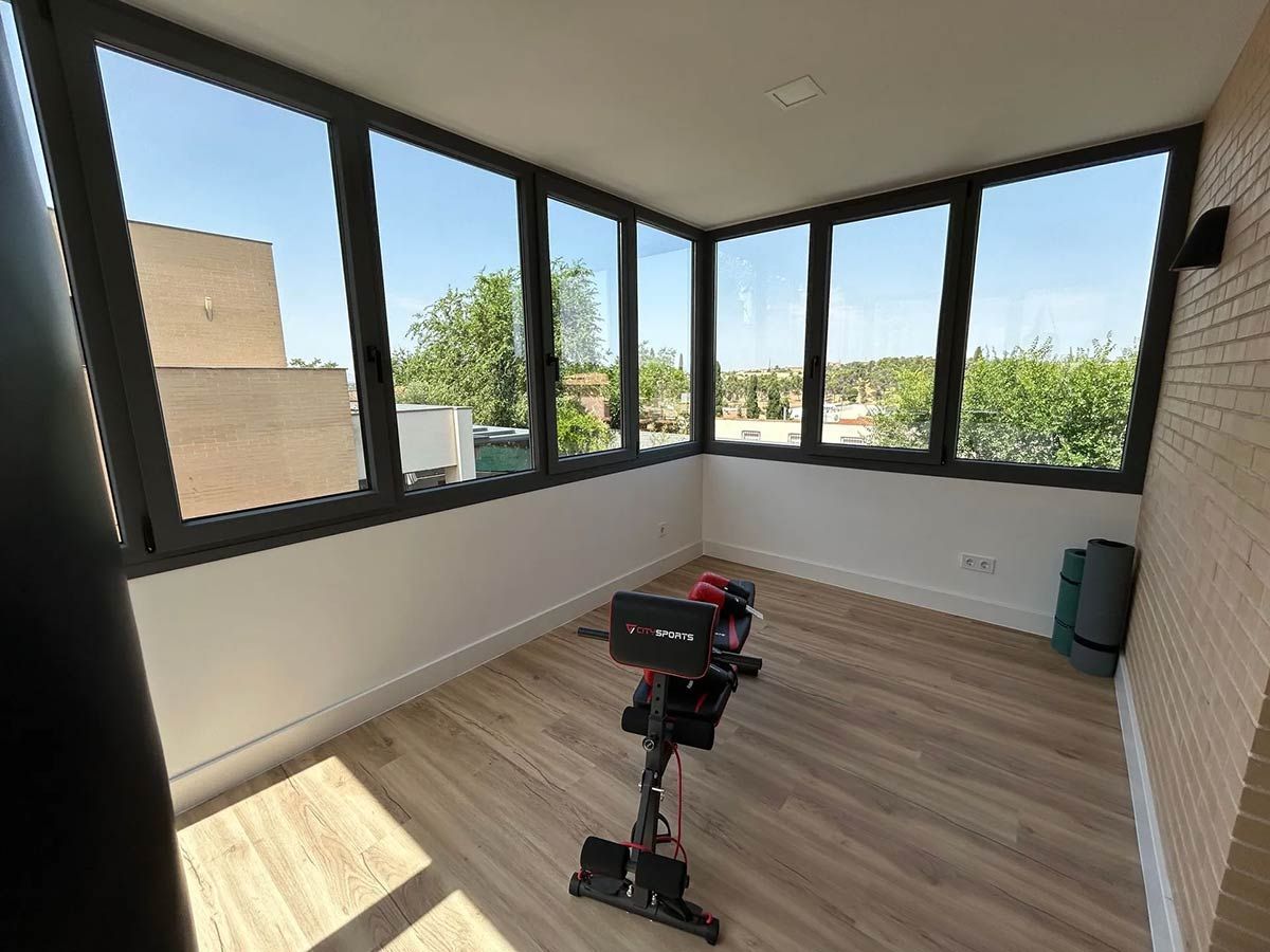 Gimnasio en casa iluminado por el sol, con máquina de remo y vista al exterior.