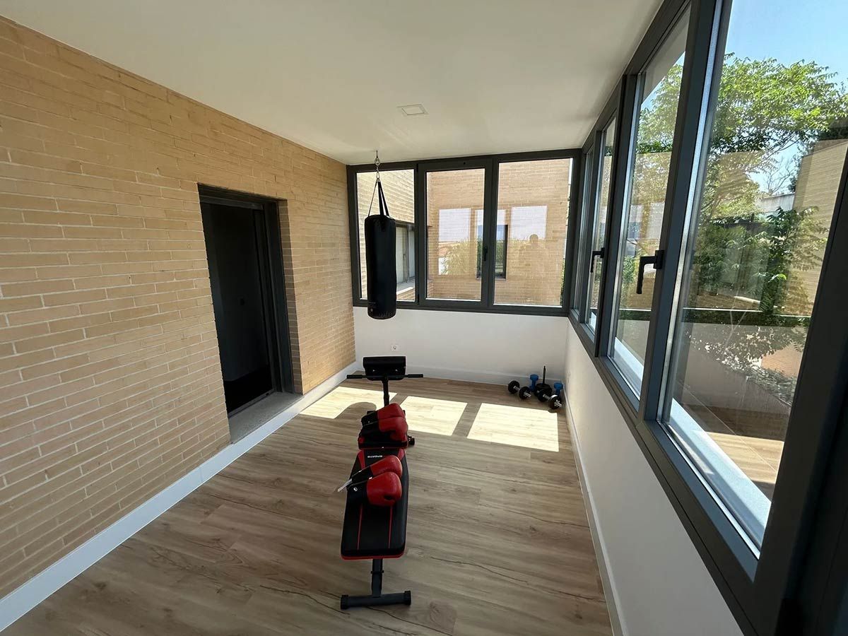 Gimnasio en casa con saco de boxeo, pesas y banco. Habitación luminosa con ventanas.