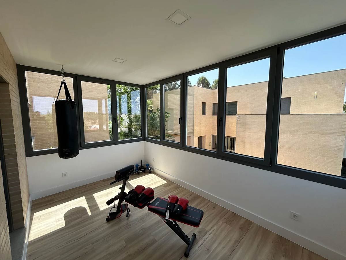 Gimnasio en casa con saco de boxeo, banco de pesas y grandes ventanales.