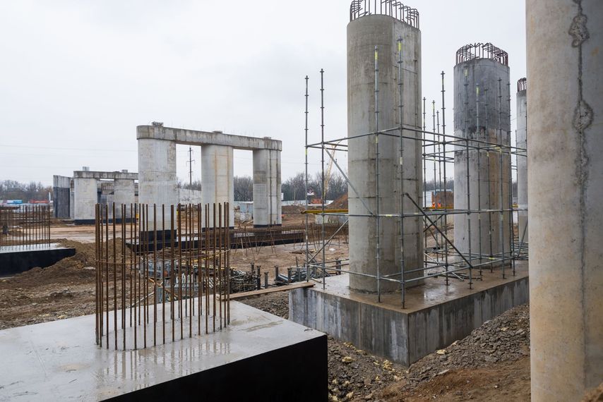 Chantier de construction avec piliers en béton, barres d'armature et échafaudages sur une fondation boueuse.